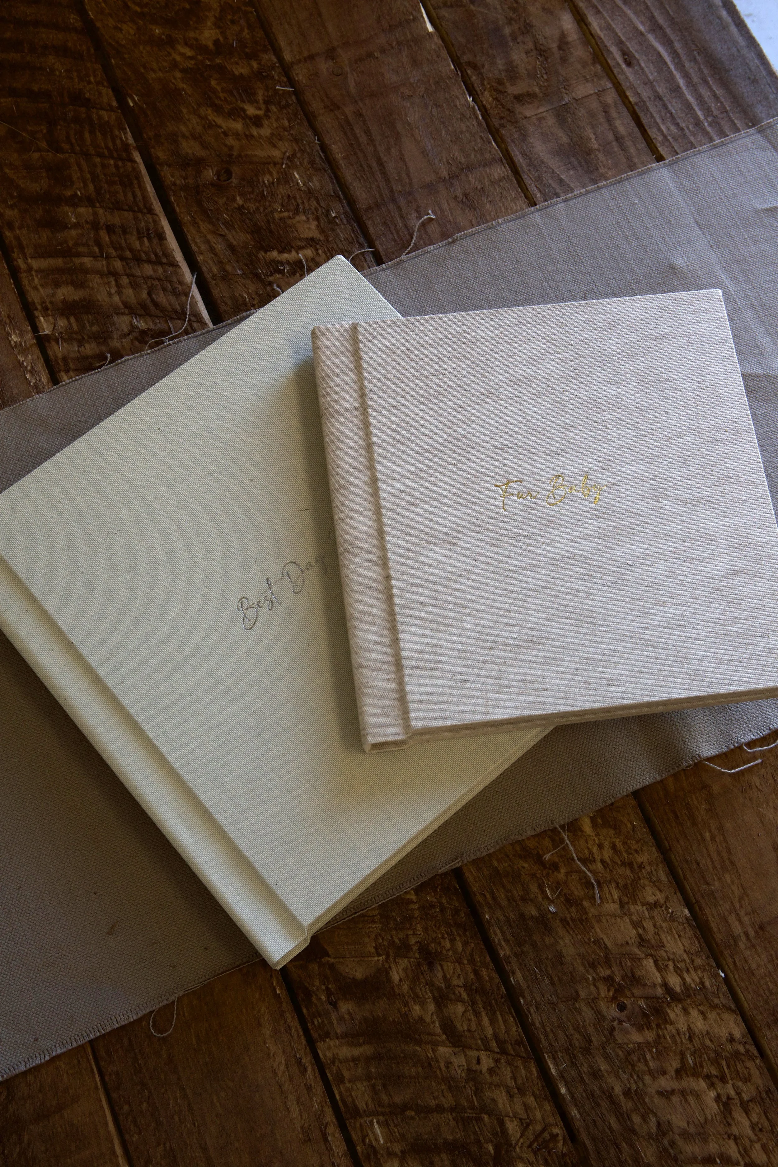 Three linen-bound photo albums on a wooden floor. The albums are labeled 'Fun Baby' and 'Best Day'.