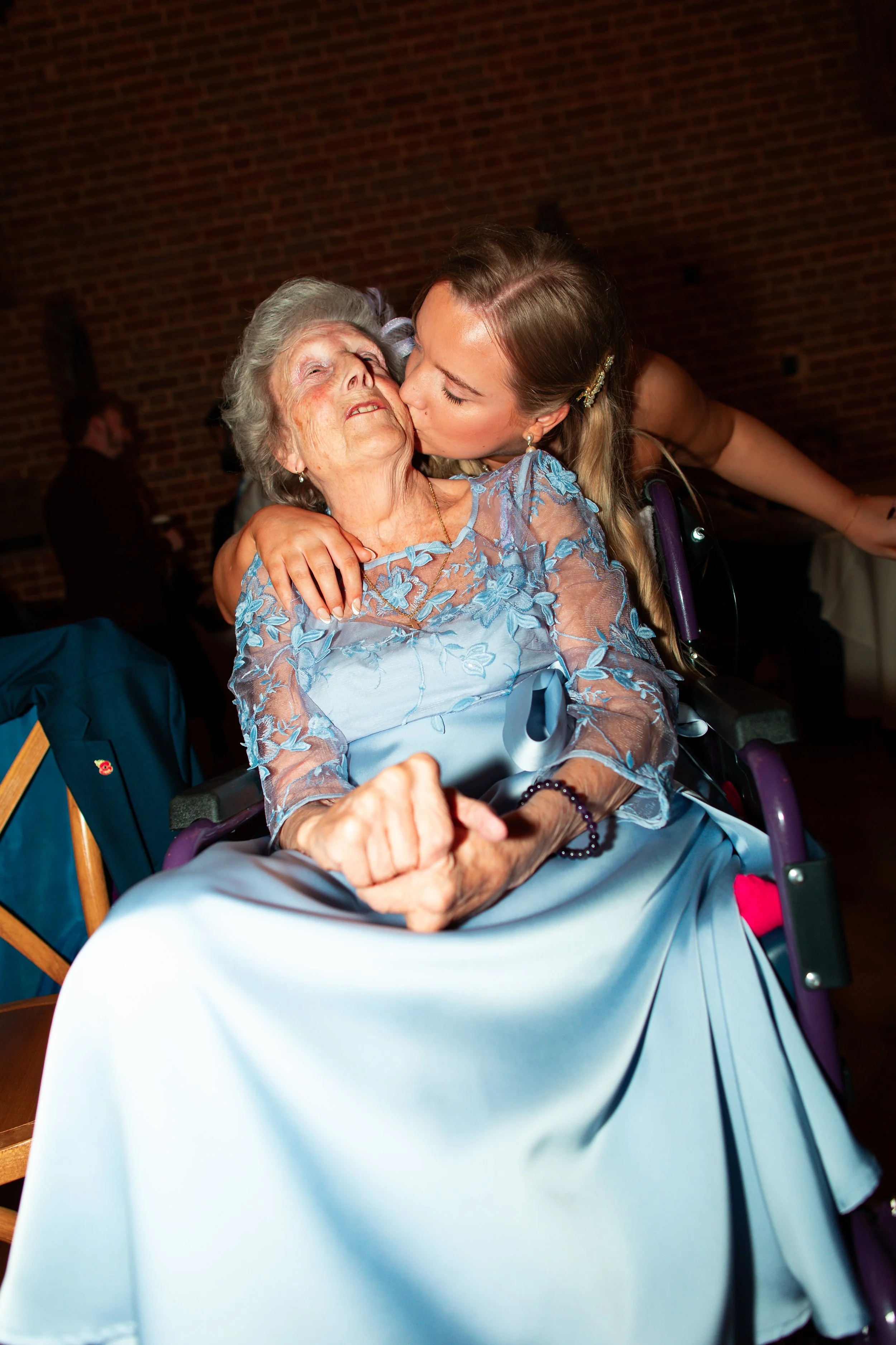 Young woman giving a loving kiss to an elderly woman in a wheelchair at a celebration event.