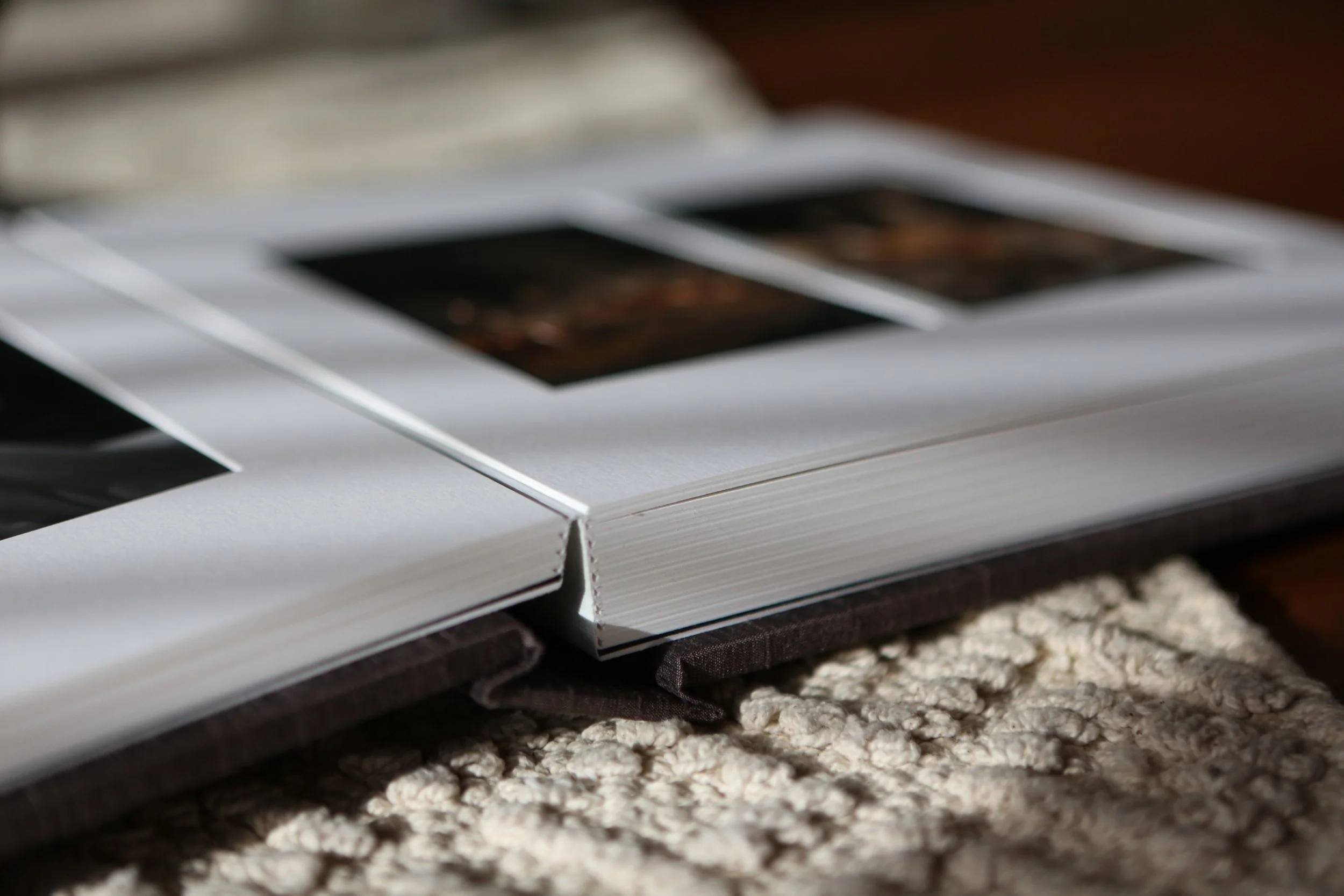 Close-up of a photo album with photographs inside, lying open on a textured beige carpet.