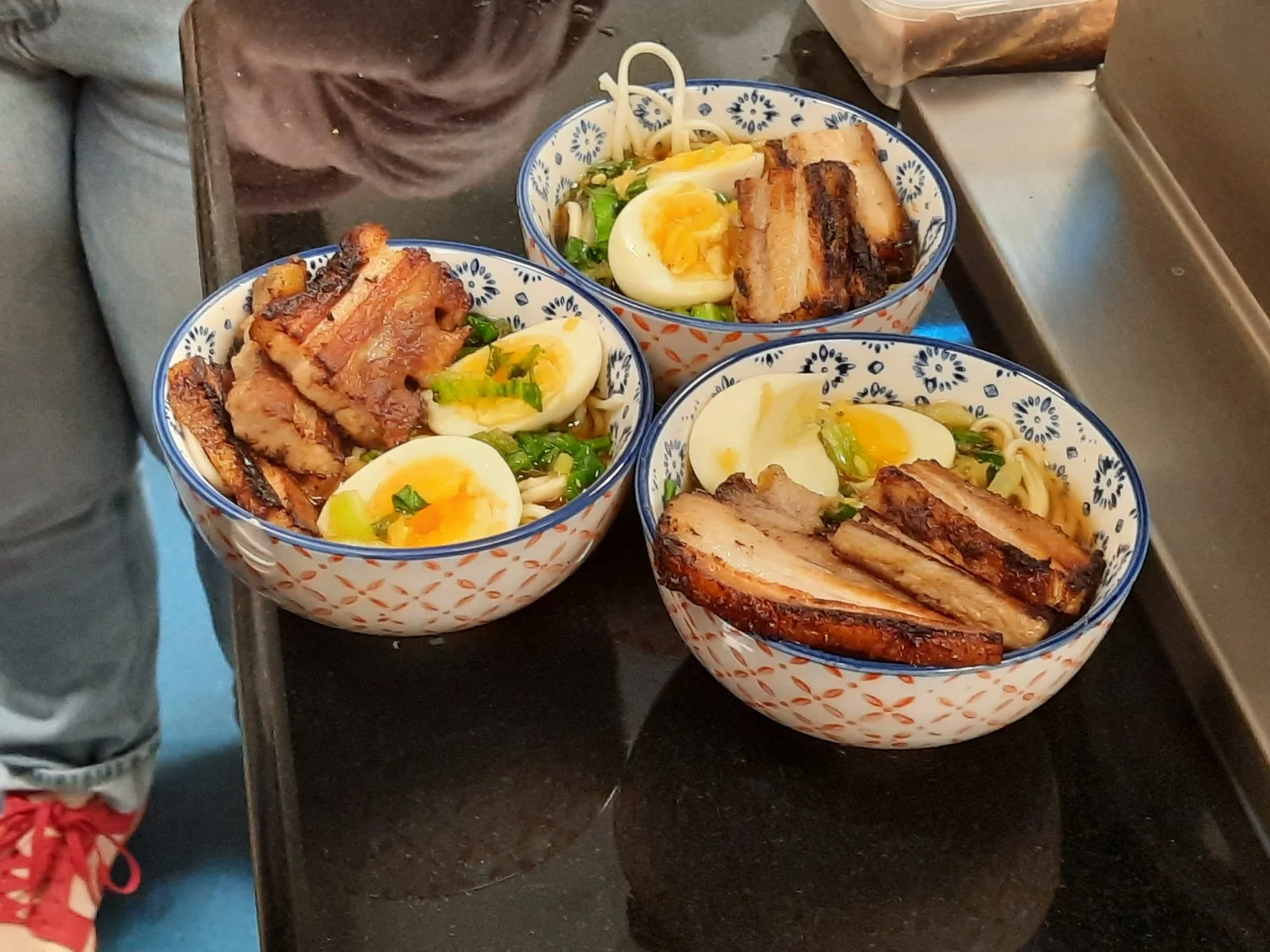 Three bowls of ramen topped with soft boiled eggs, grilled pork belly, and green onions.
