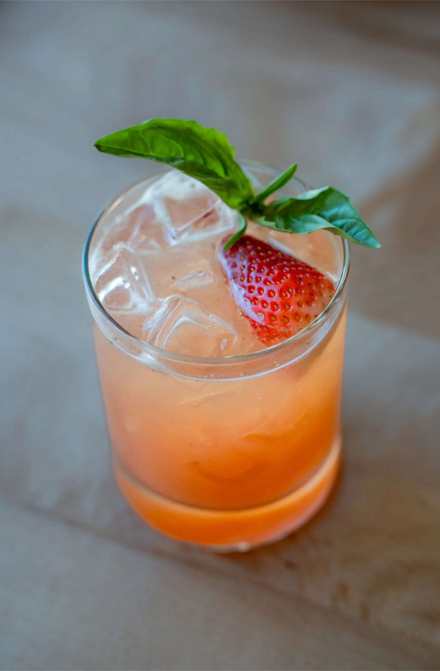 A glass of pink iced drink garnished with a strawberry and a basil leaf.
