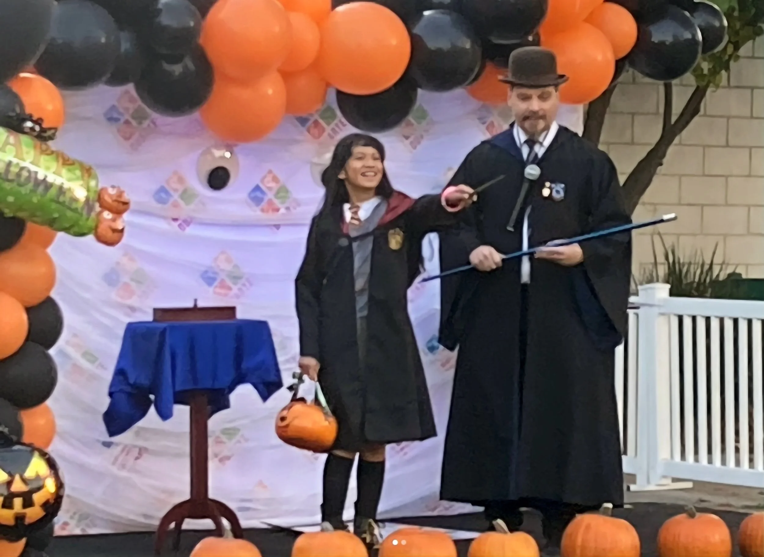 John on Stage in his Ravenclaw robe at Duarte's Halloween Howl with a young lady in a Gryffindor robe enthusiastically pointing her wand.