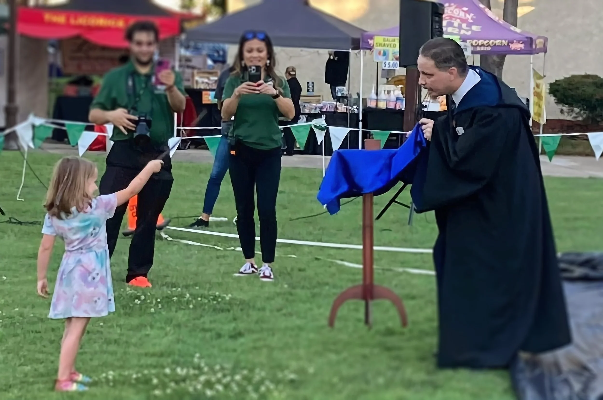 John at outdoor Chino Summer movie nights in his Ravenclaw robe with a young child holding a wand as a table floats off the ground.