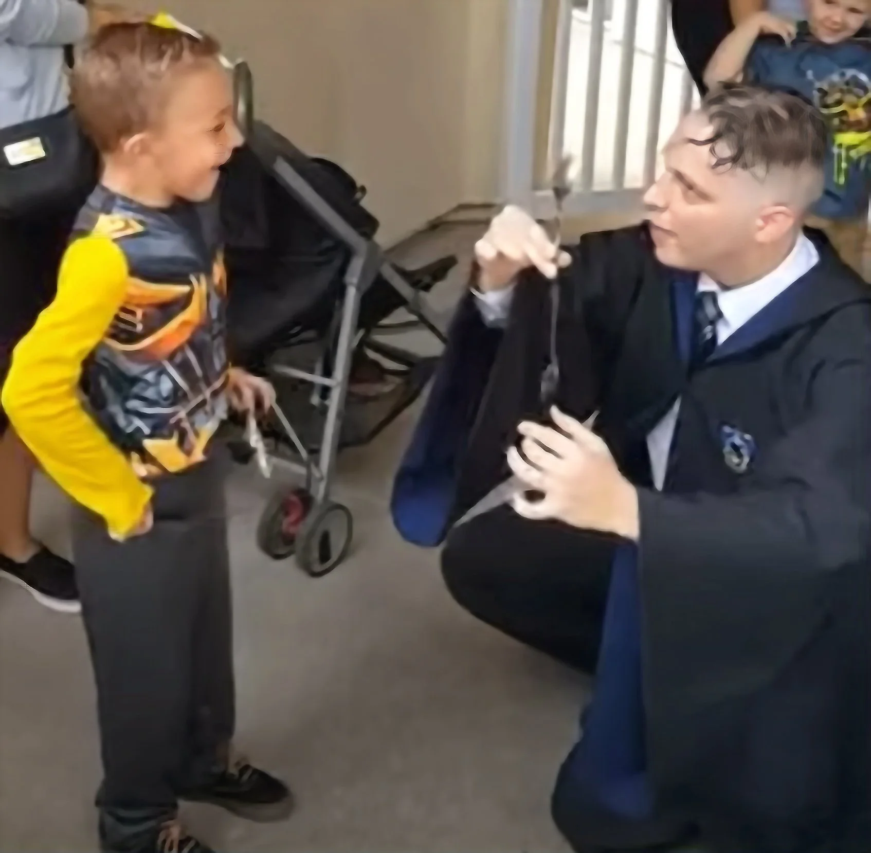 John is holding two spoons one seemingly levitating in mid air as John is holding one spoon up and the spoon down is floating directly blow. A child smiles widely as he had just waved his wand to make the magic happen. 