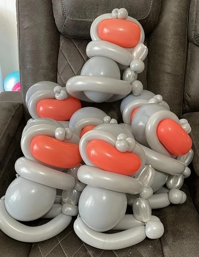 An arrangement of balloons shaped like ducks, predominantly in white and orange, placed on a brown couch.