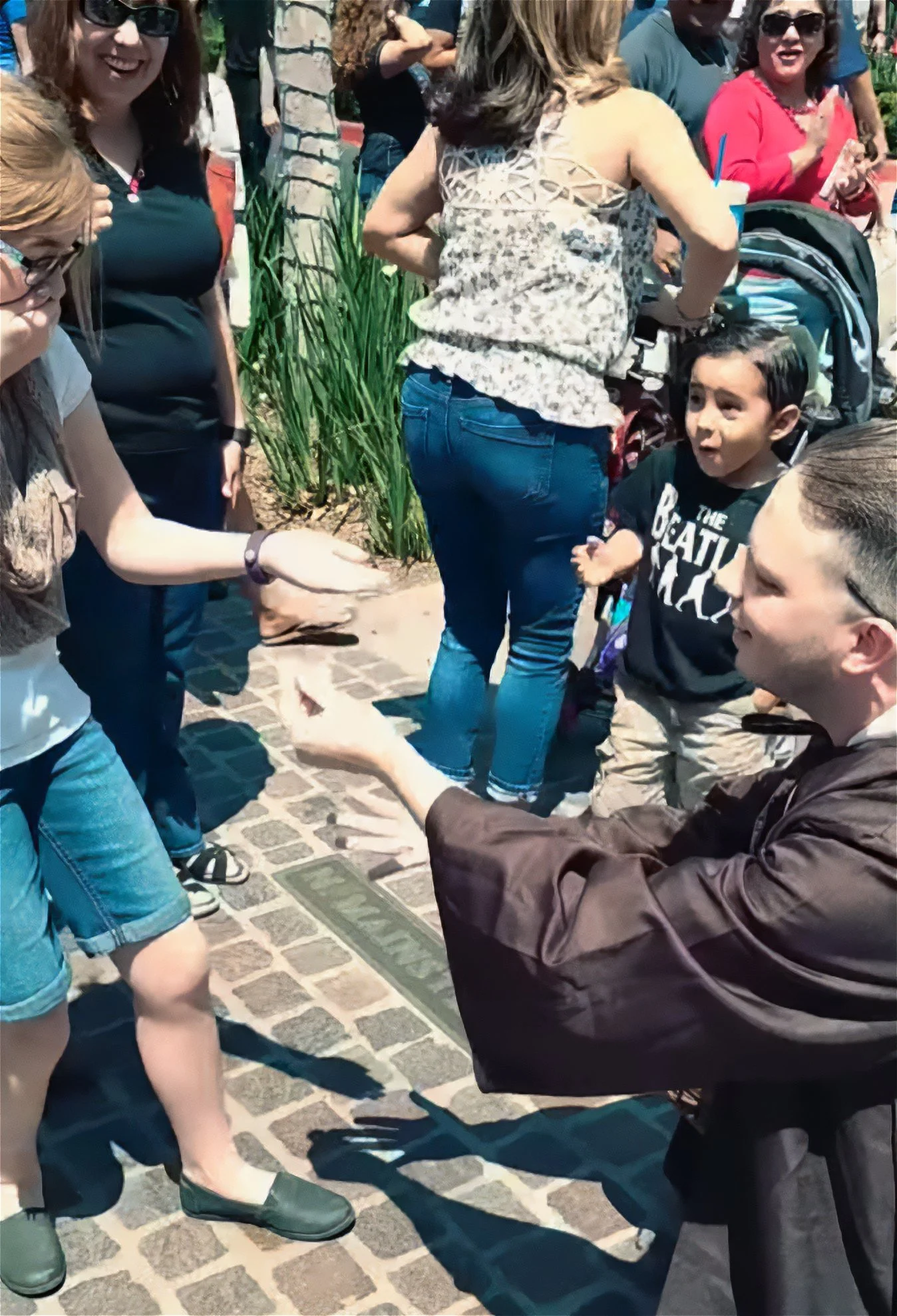 John in his Obi John Kenobi costume amazes a young girl who is gasping with her mouth covered with her right hand as she looks at her left hand which has opened and items have changed. An onlooker male child gasps as well