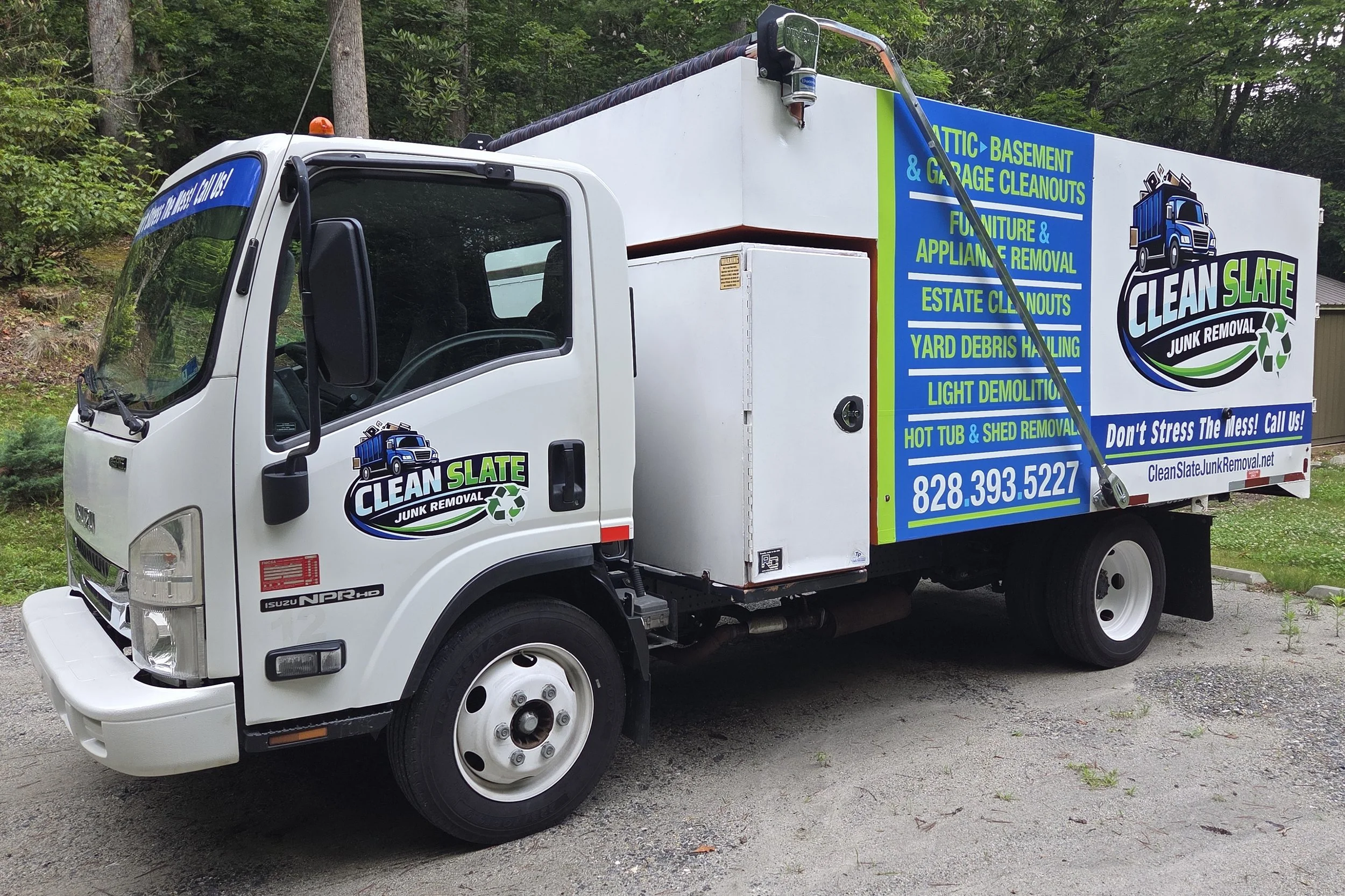 A white junk removal truck with a colorful advertisement on the side listing services such as attic, basement, and garage cleanouts, furniture and appliance removal, yard debris hauling, and light demolition. The truck has a blue, green, and black logo with the text 'Clean Slate Junk Removal' and a recycling symbol.