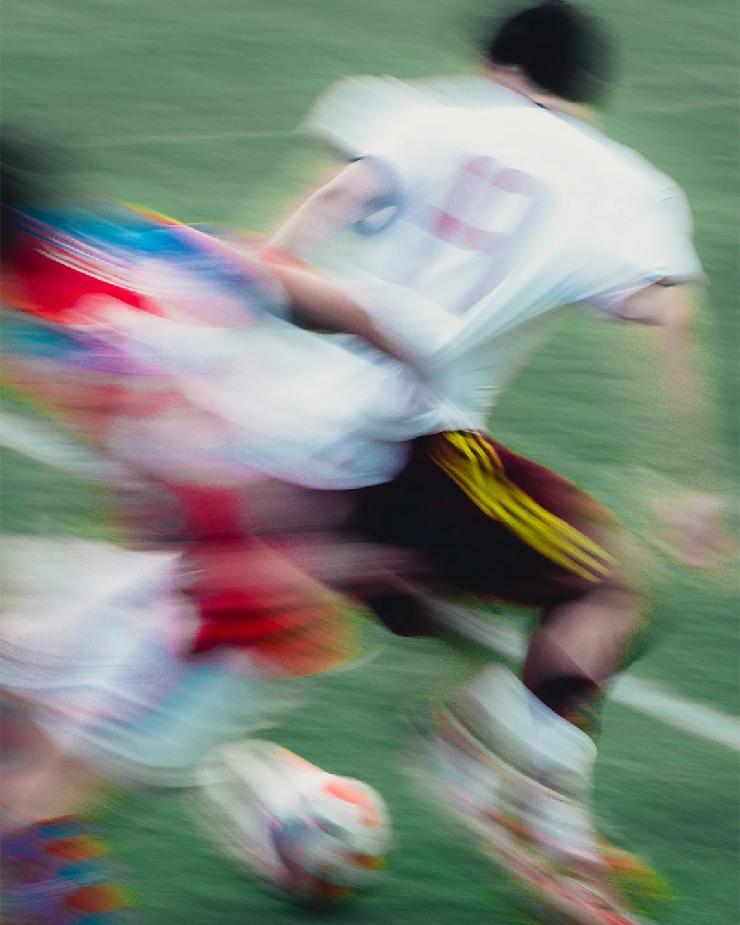 Blurred motion image of a soccer player running on a field wearing a white shirt, black shorts with yellow stripes, and colorful shoes, holding a soccer ball.
