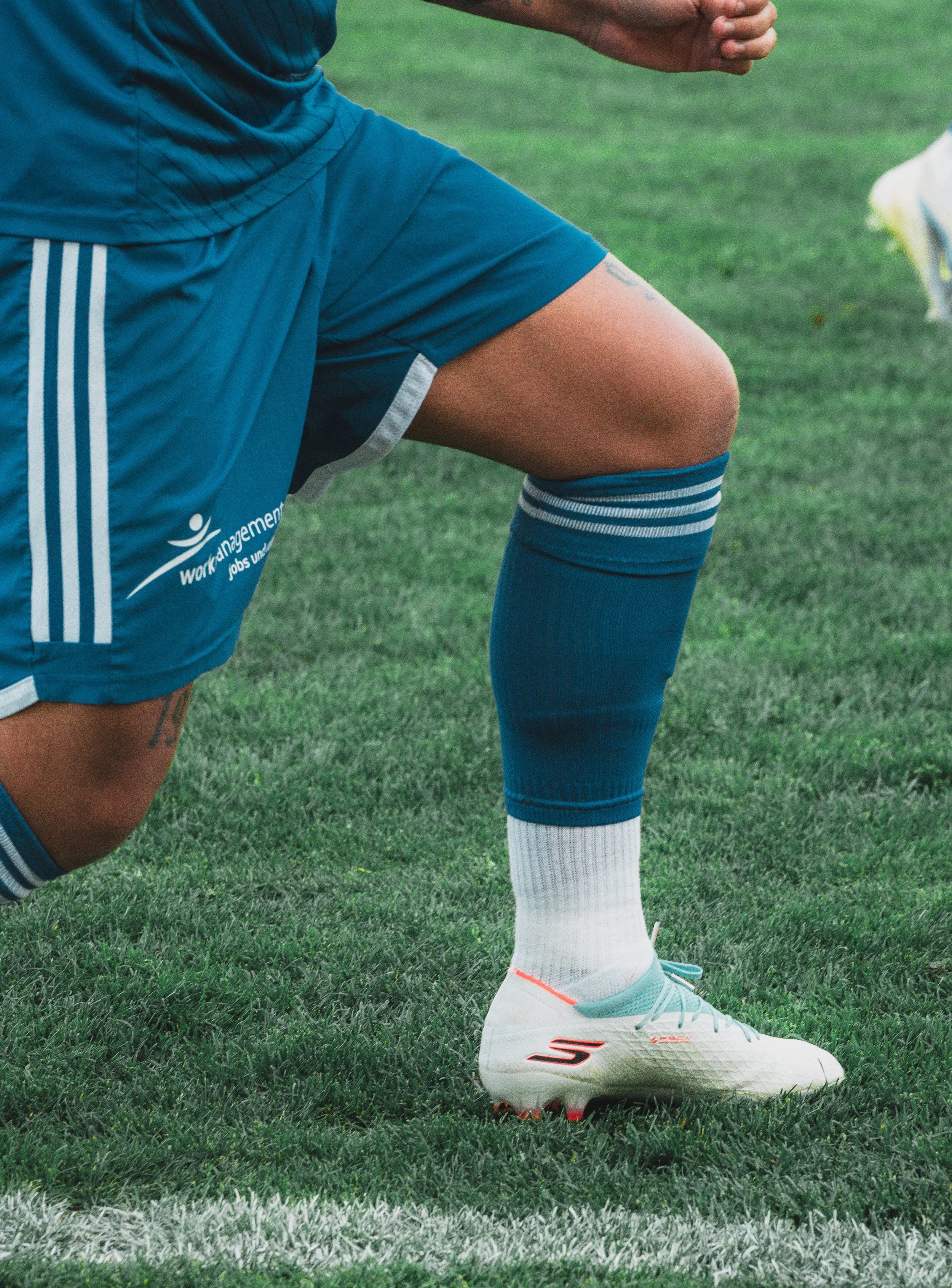Close-up of a person's lower body, wearing blue athletic shorts, socks, and white soccer cleats, on a green grass field.