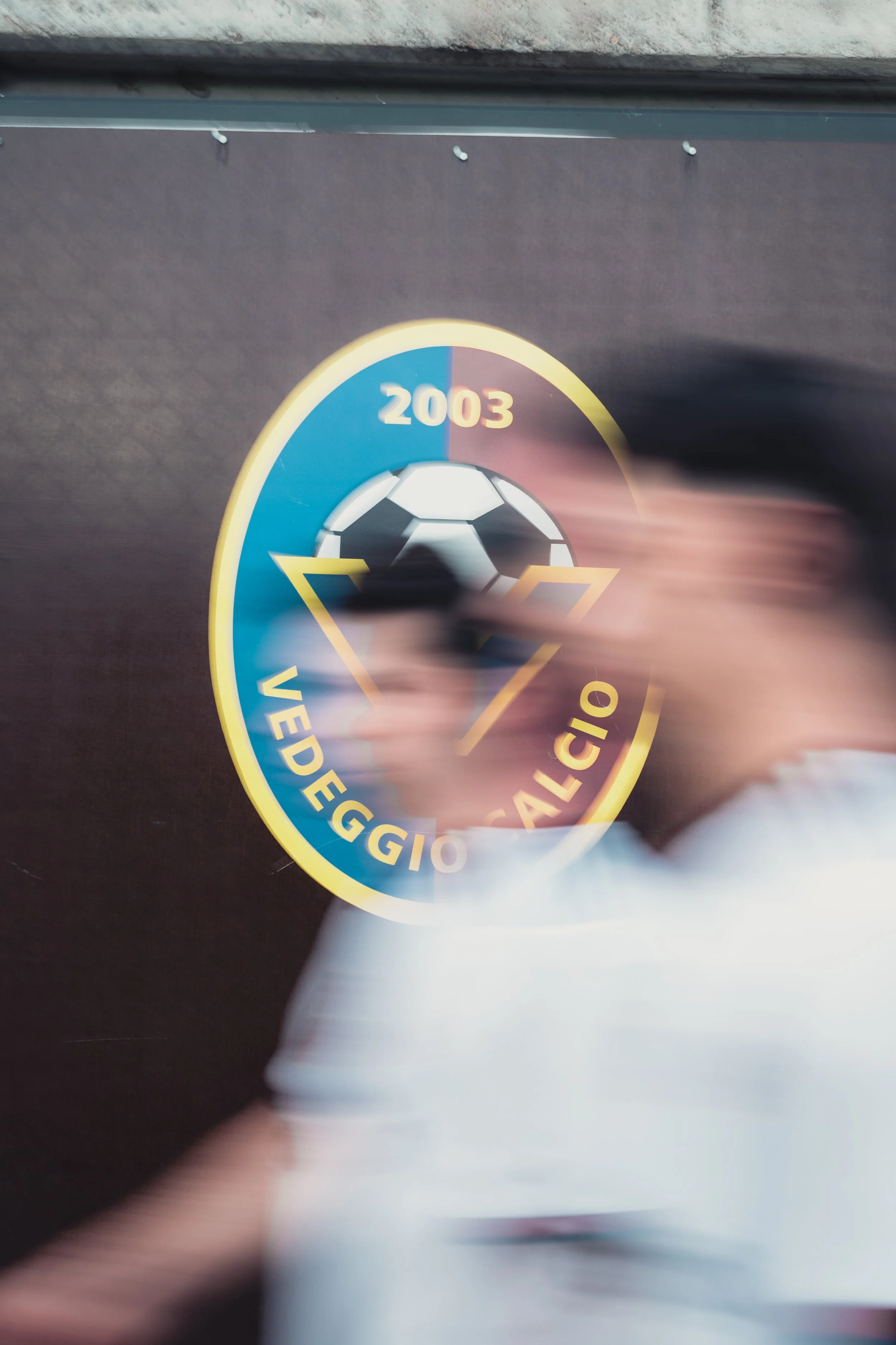 Blurry photo of a circular logo with a soccer ball in the center, surrounded by text that includes the words "Vig", "DS", and "2003" on a dark background.