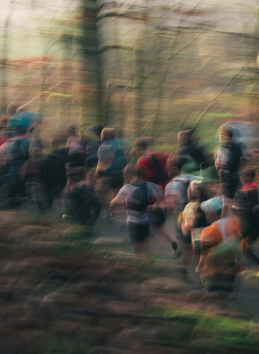 Blurry photo of a crowd of people walking outdoors, with trees in the background.