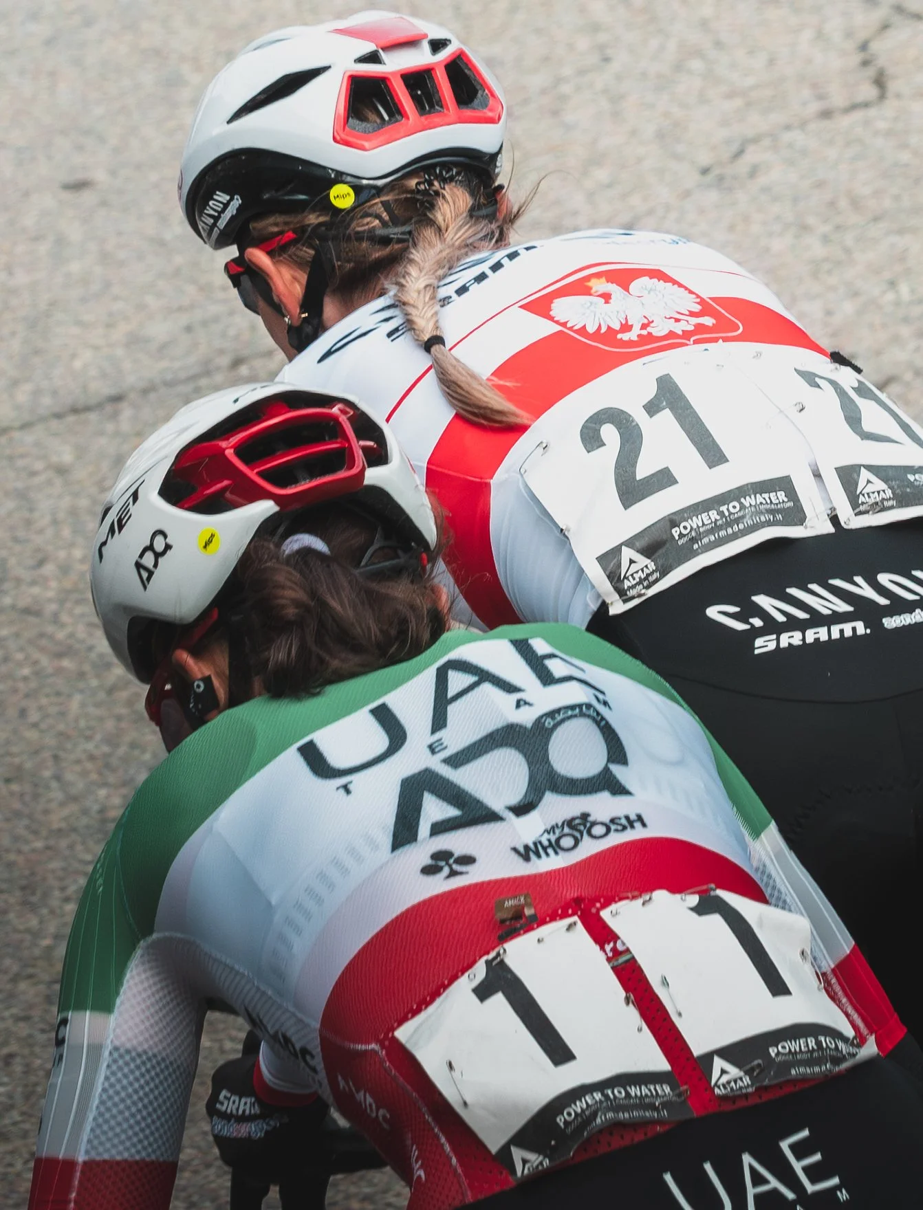 Close-up of three cyclists in a race, wearing helmets and colorful uniforms, leaning forward in a position of exertion.