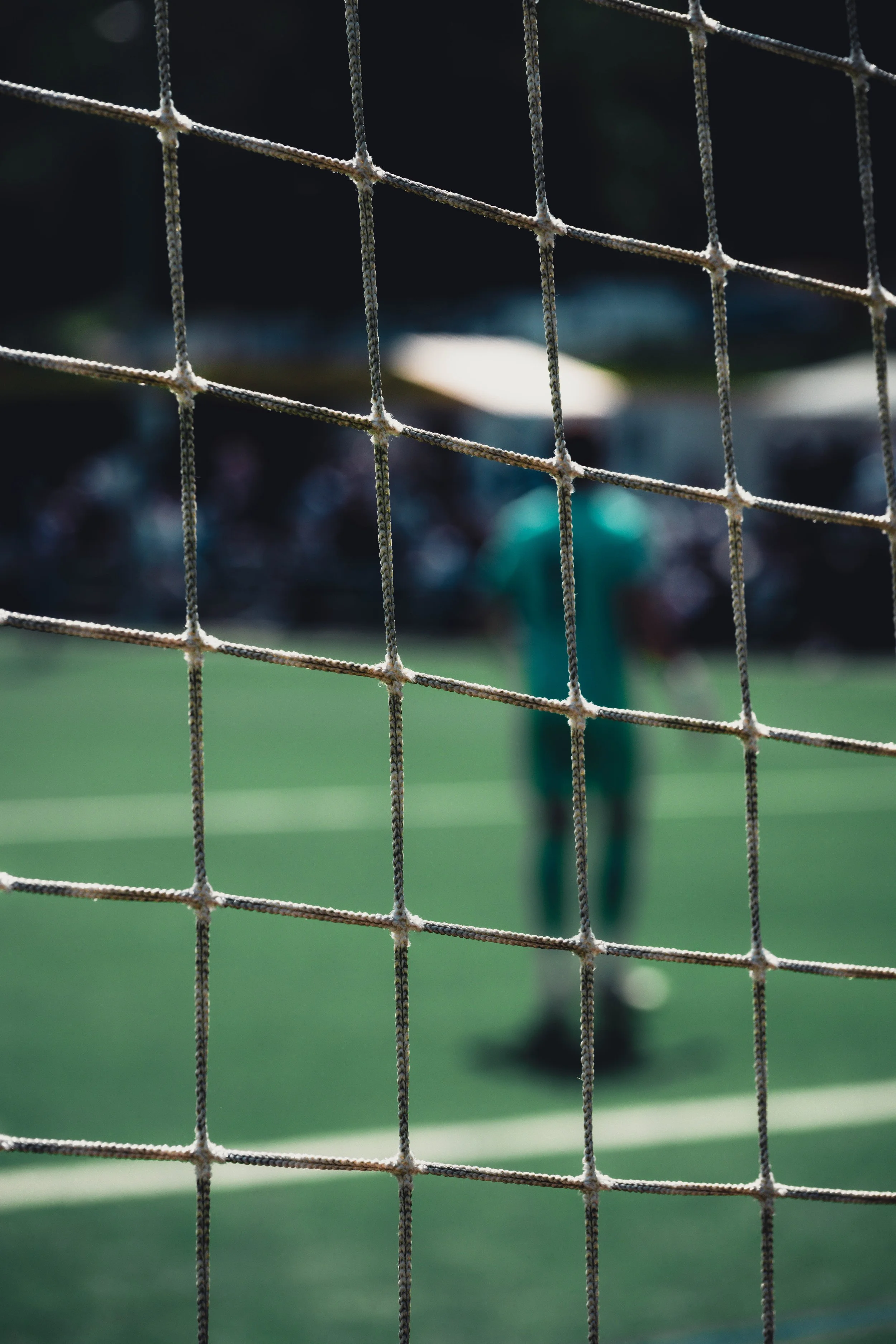 Close-up of a tennis net with a blurred tennis player and green court in the background.