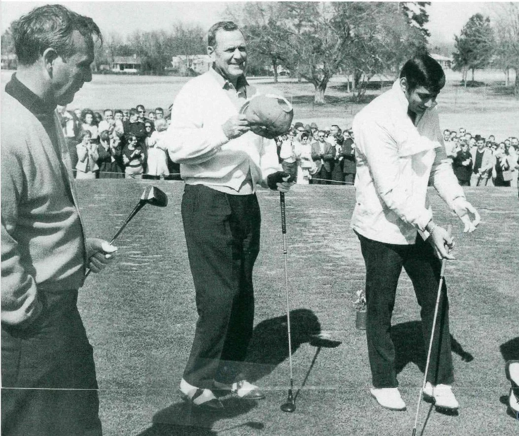 Three men standing on a golf course preparing to play golf, with a crowd of spectators in the background.