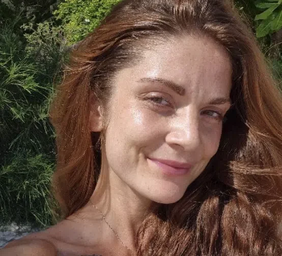 Close-up of woman with long red hair outdoors, smiling slightly at camera.