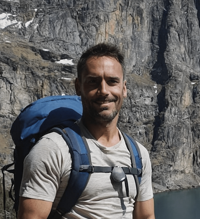 Man hiking outdoors with a backpack in mountainous terrain near a body of water.