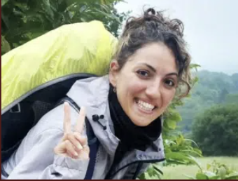 Young woman hiking outdoors, smiling and flashing a peace sign.