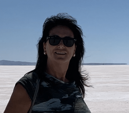 Woman with sunglasses and earrings smiling outdoors near a salt flat
