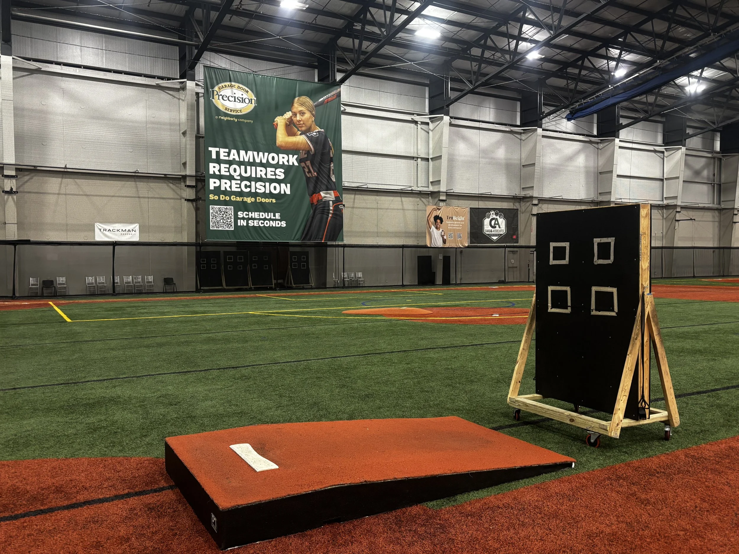 Indoor sports facility with green artificial turf, advertising banners, target practice platform, and track equipment.