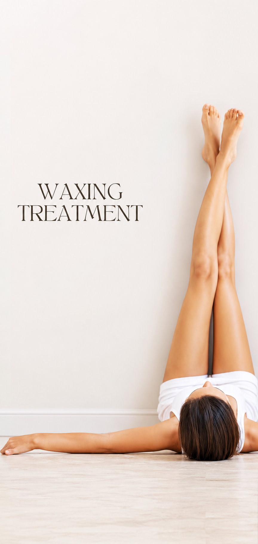 A woman lying on the floor with her legs raised against a wall, receiving a waxing treatment.