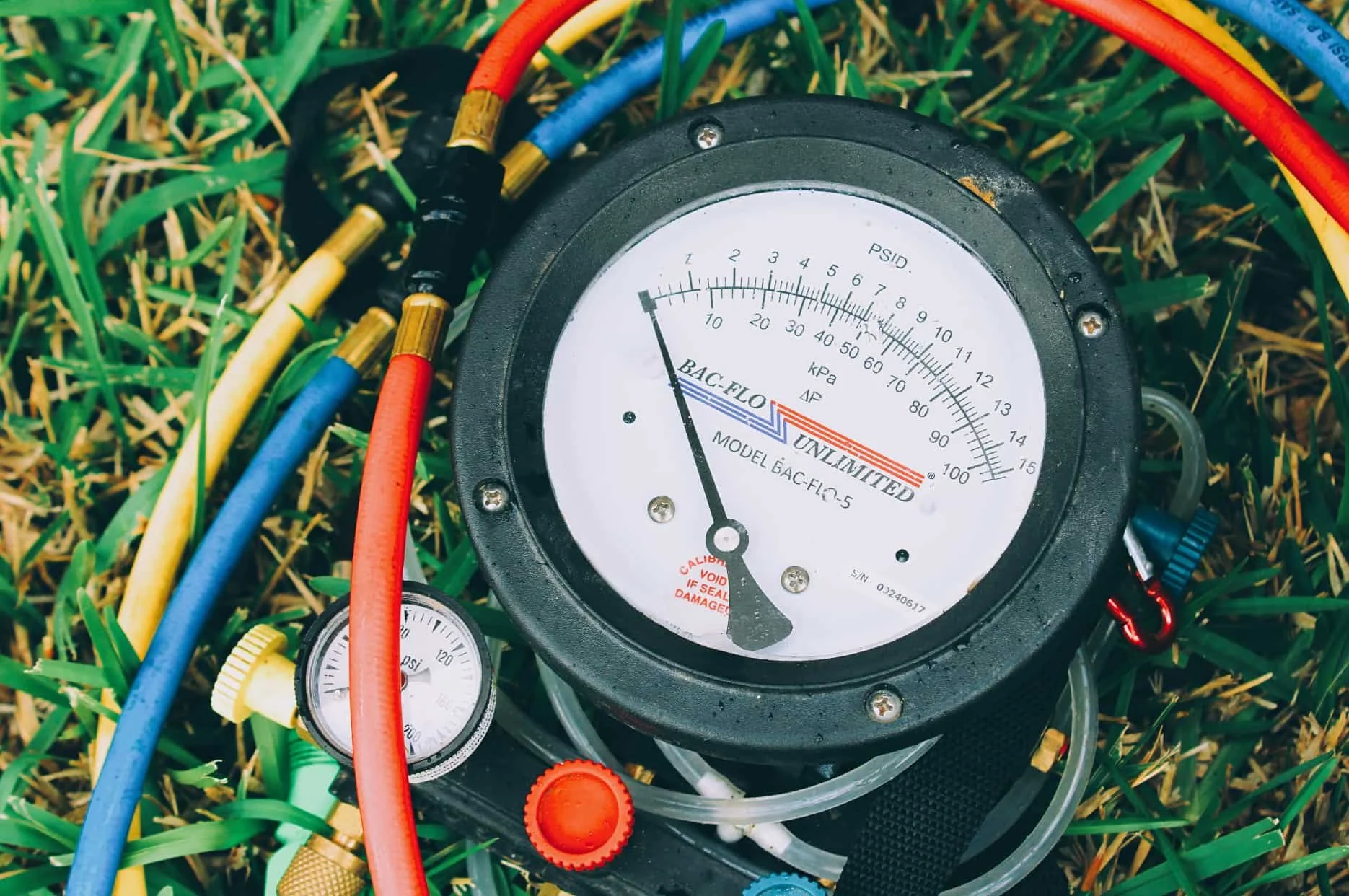 A pressure gauge with various colored hoses connected, lying on green grass.