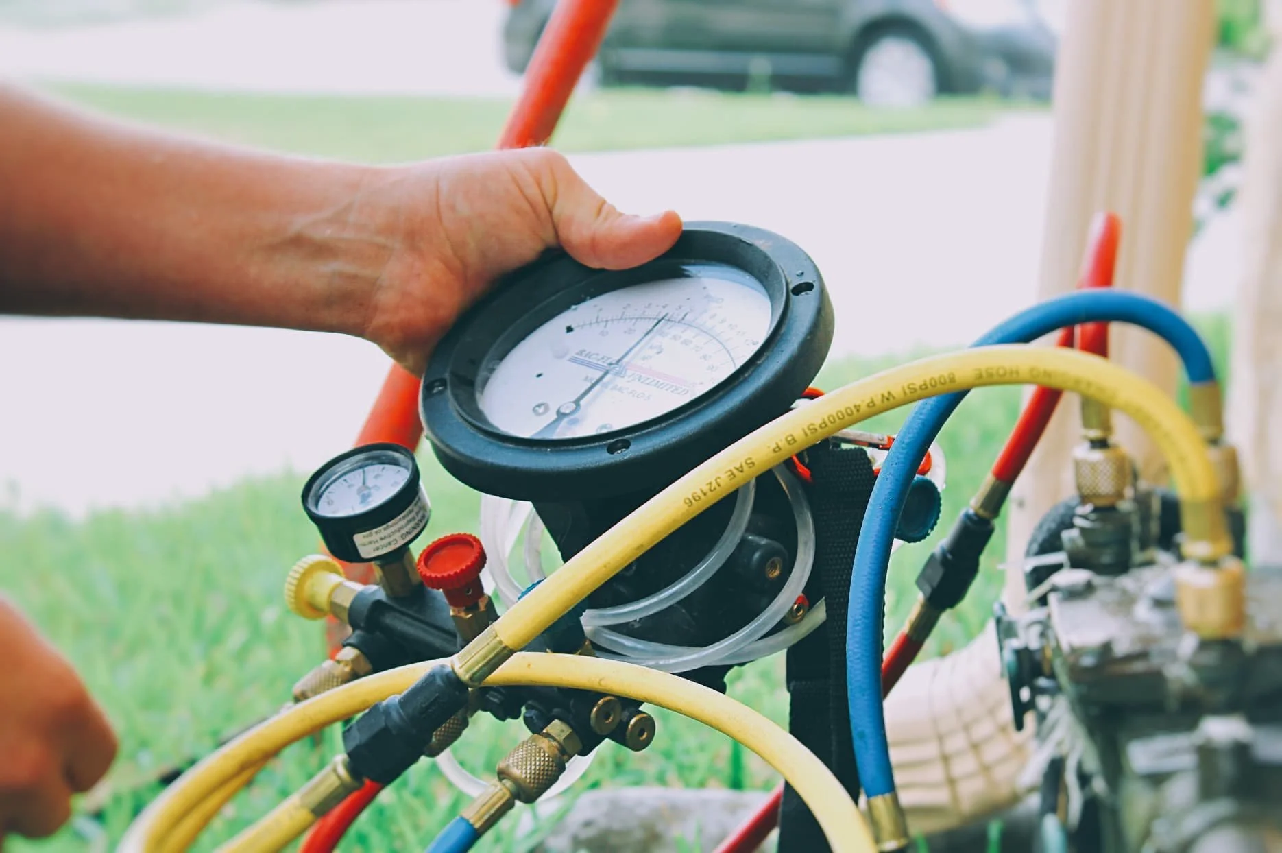 Person testing pressure of a refrigeration or air conditioning system using gauges connected to blue and yellow hoses.