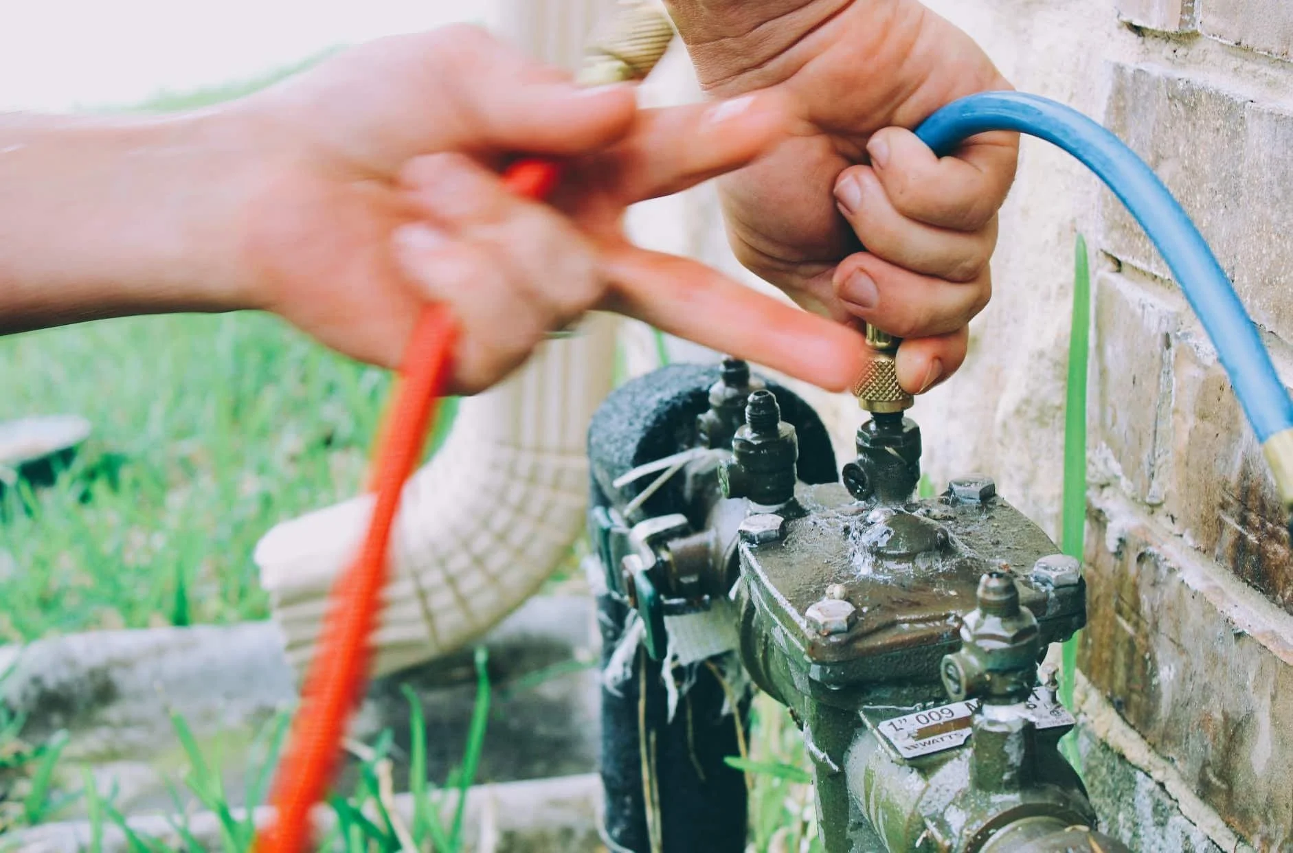 Person using a wrench to tighten a pipe connection outside on a brick wall.