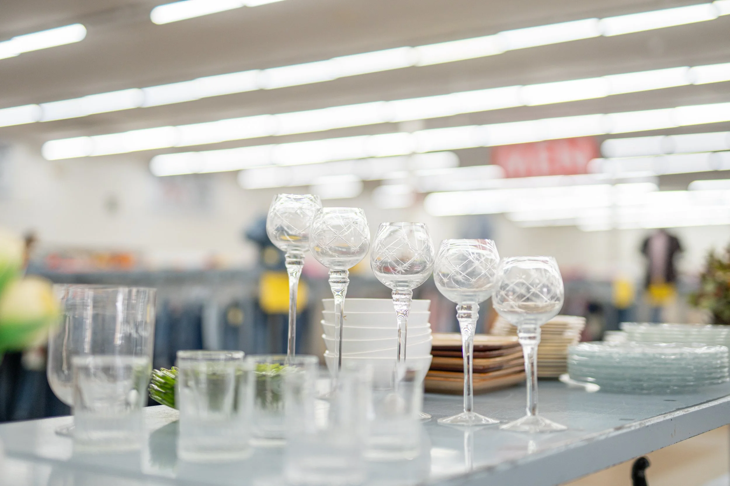 Clear glassware displayed on a store shelf, with overhead fluorescent lighting in the background.