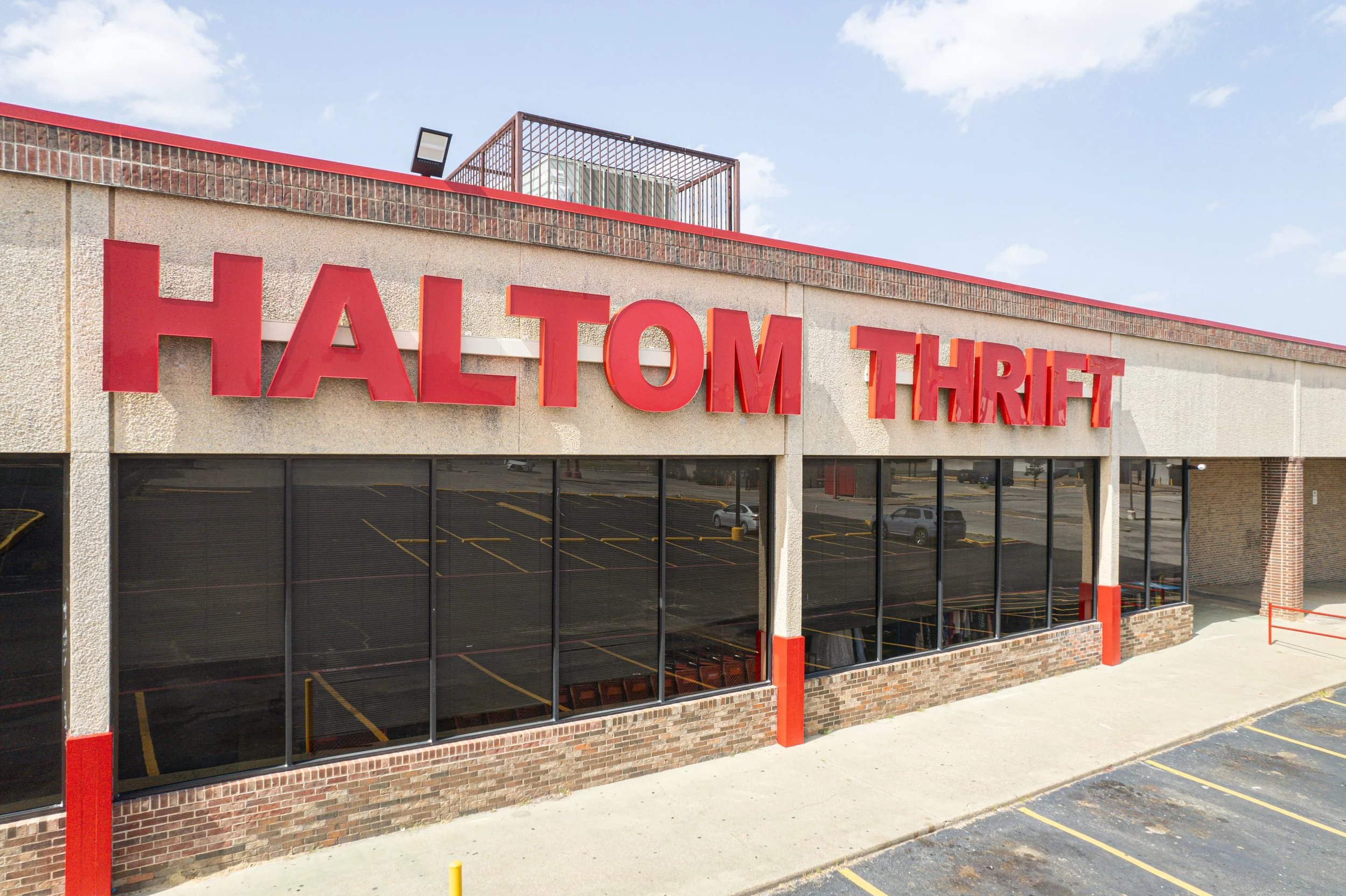 Exterior of a building with 'Haltom Thrift' sign, featuring large glass windows and a parking lot.