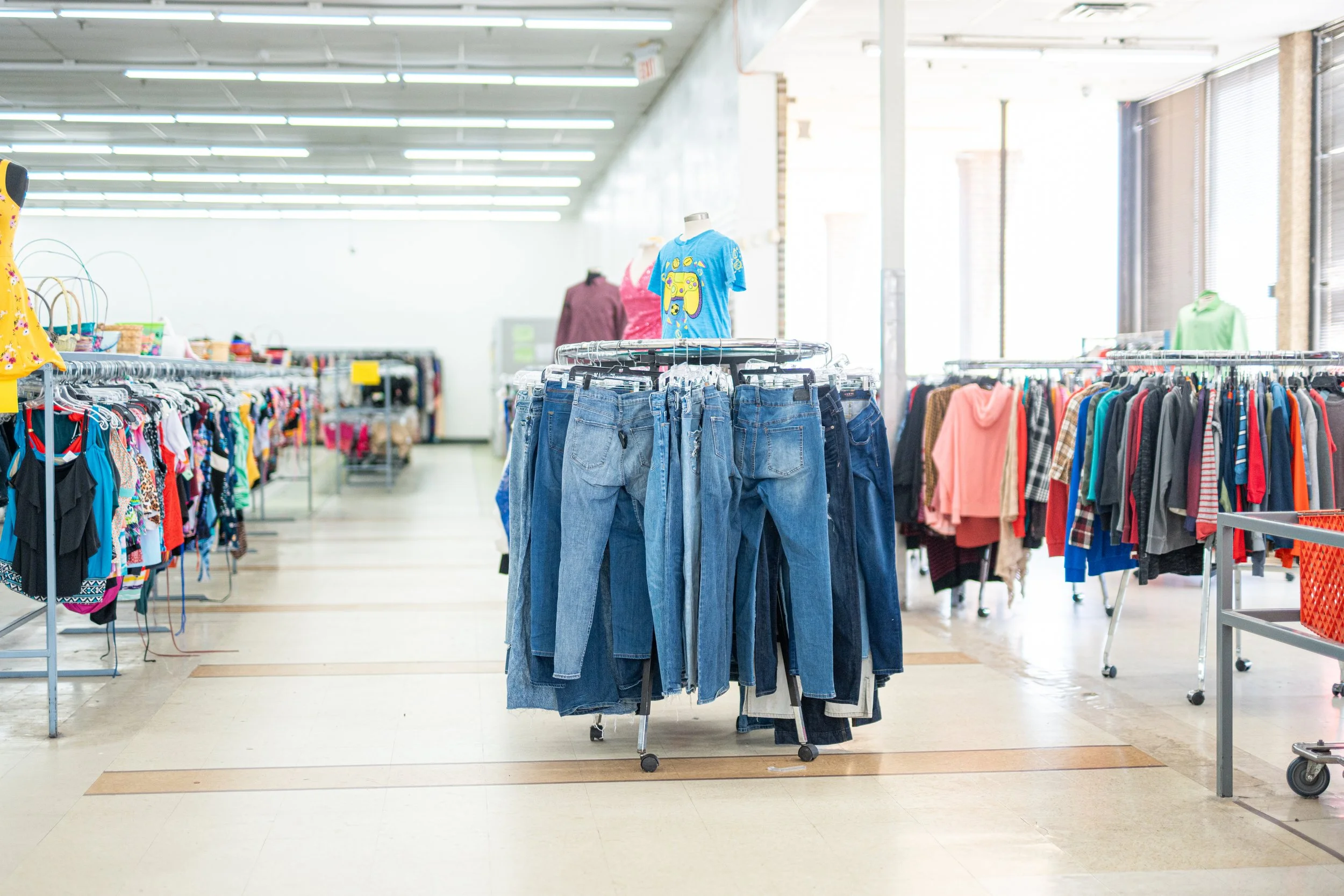 Thrift store interior with clothing racks displaying jeans and colorful tops.