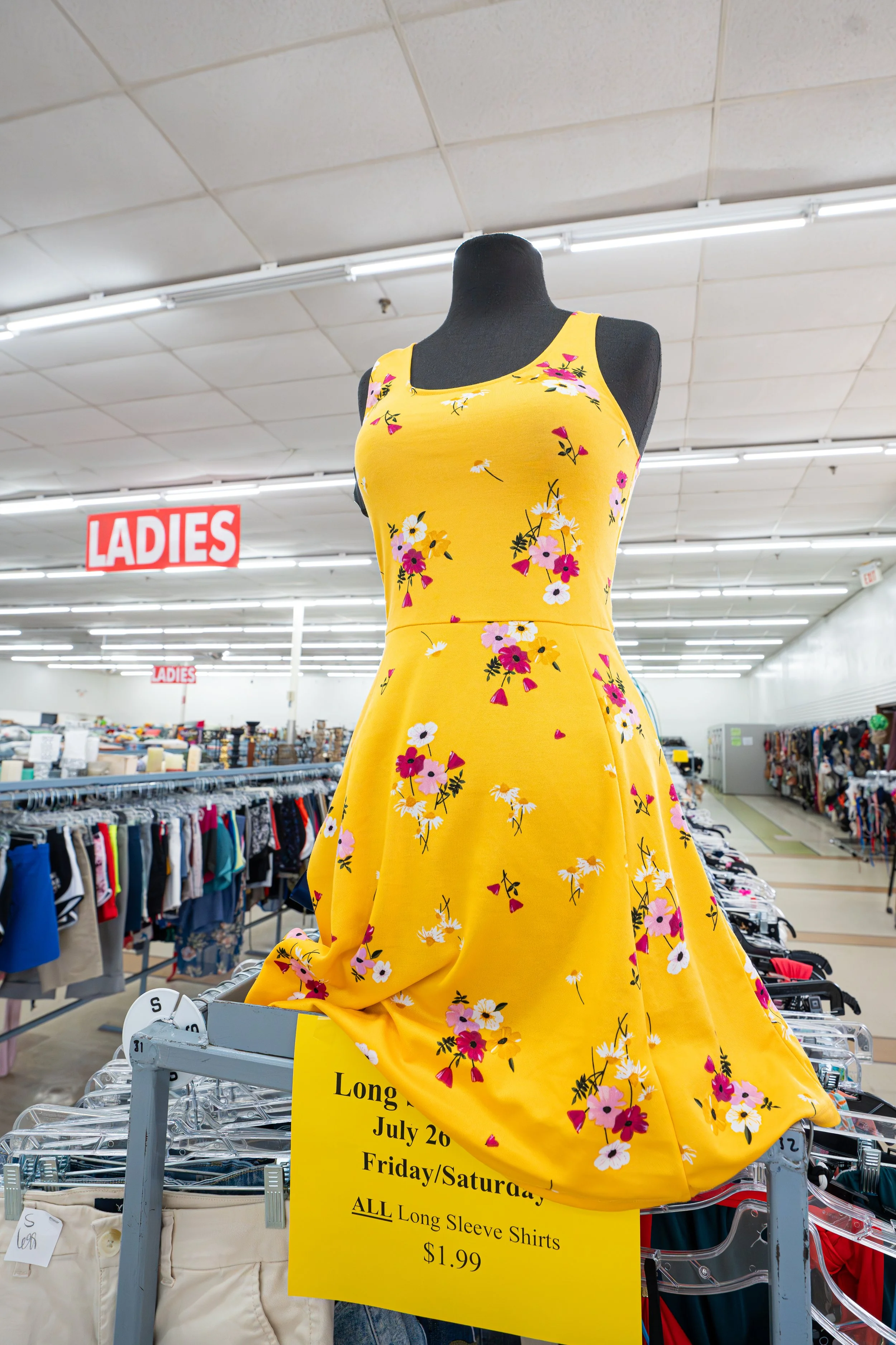 Mannequin wearing a yellow floral dress in a clothing store with a "Ladies" sign in the background.