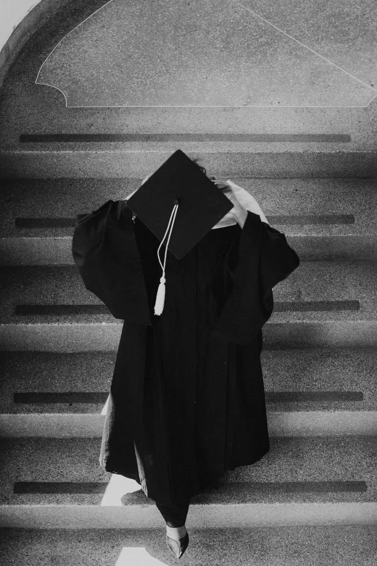 Joven con toga de graduación, sombrero y zapatos de tacón, caminando por unas escaleras.