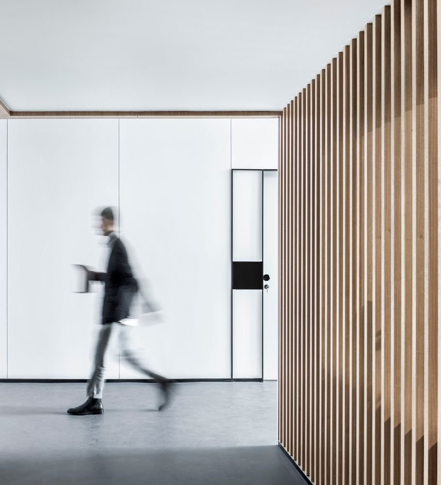 Persona caminando dentro de una oficina moderna, con paredes blancas y una pared de listones de madera en el lado derecho