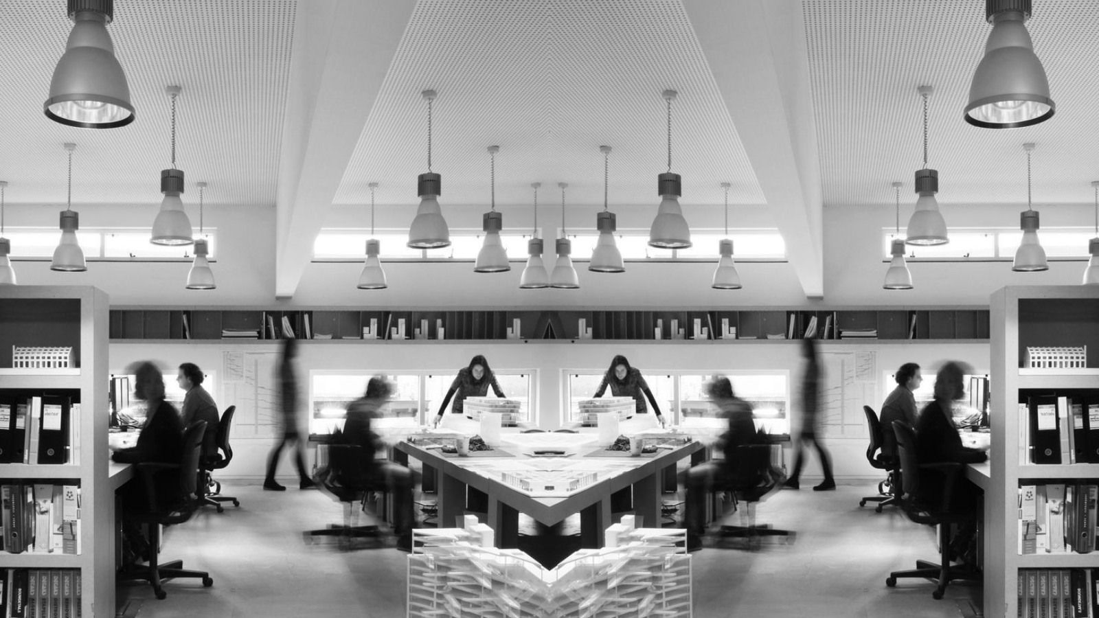 oficina moderna con libros, escritorios y empleados trabajando, vista de sala con iluminación blanca y estructura arquitectónica de diseños simples