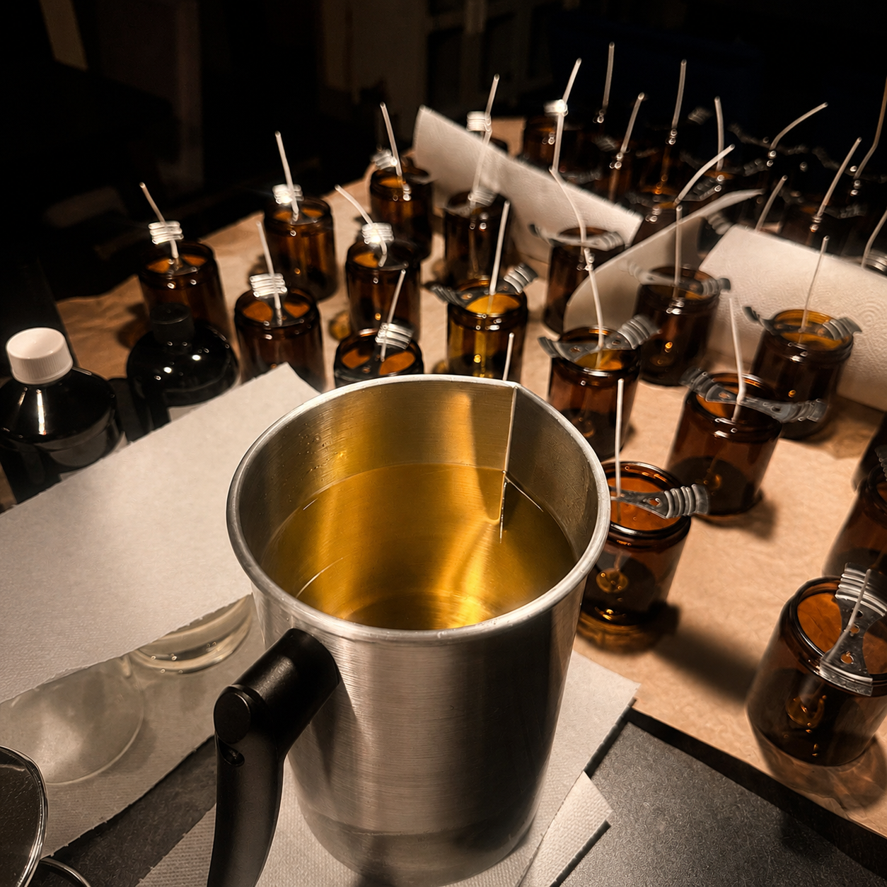 Amber glass bottles with white straws, a stainless steel pitcher, and bottles of black liquid on a table, suggesting a preparation process.