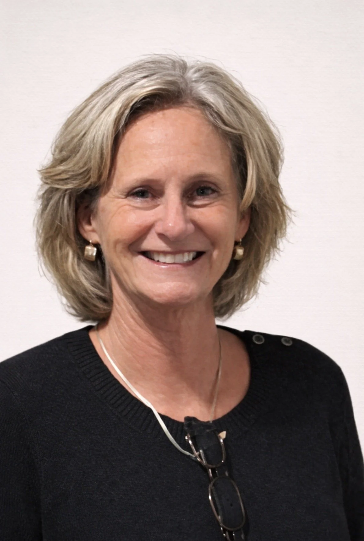 A woman with long hair sitting on a park bench, smiling at the camera, in an outdoor park setting.