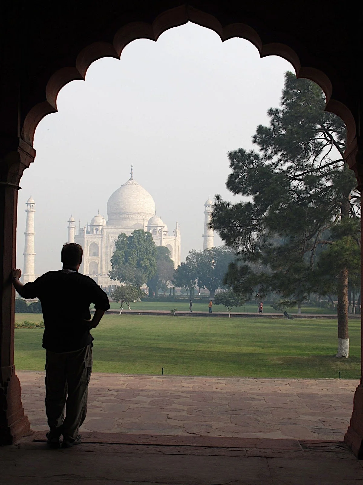 Person standing and looking at the Taj Mahal through an arched window in India.