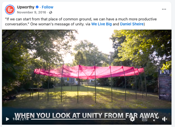 Pink fabric canopy supported by thin poles set up on a grassy area under trees in a park.