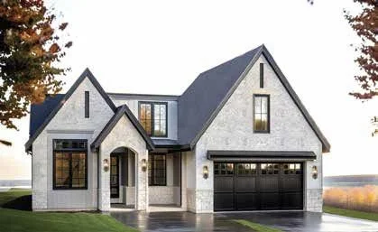 Modern two-story house with gray brick exterior and black garage door, surrounded by trees and a well-maintained lawn.