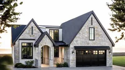 Front view of a modern two-story house with a stone facade, black roof, and attached garage, surrounded by trees.
