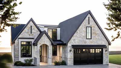 Front view of a modern two-story house with a stone facade, black roof, and attached garage, surrounded by trees.
