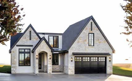 Front view of a modern two-story house with a dark gray roof, stone exterior, large windows, and an attached garage.
