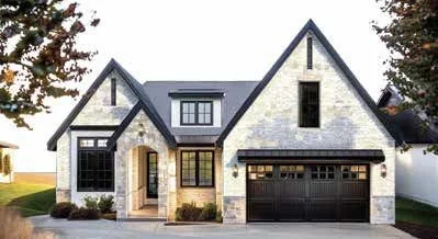 A modern two-story house with a stone exterior, dark gray roof, and black garage door, surrounded by trees.