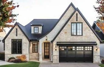 Modern house with stone and stucco exterior, a garage, and a steep gabled roof, surrounded by trees.