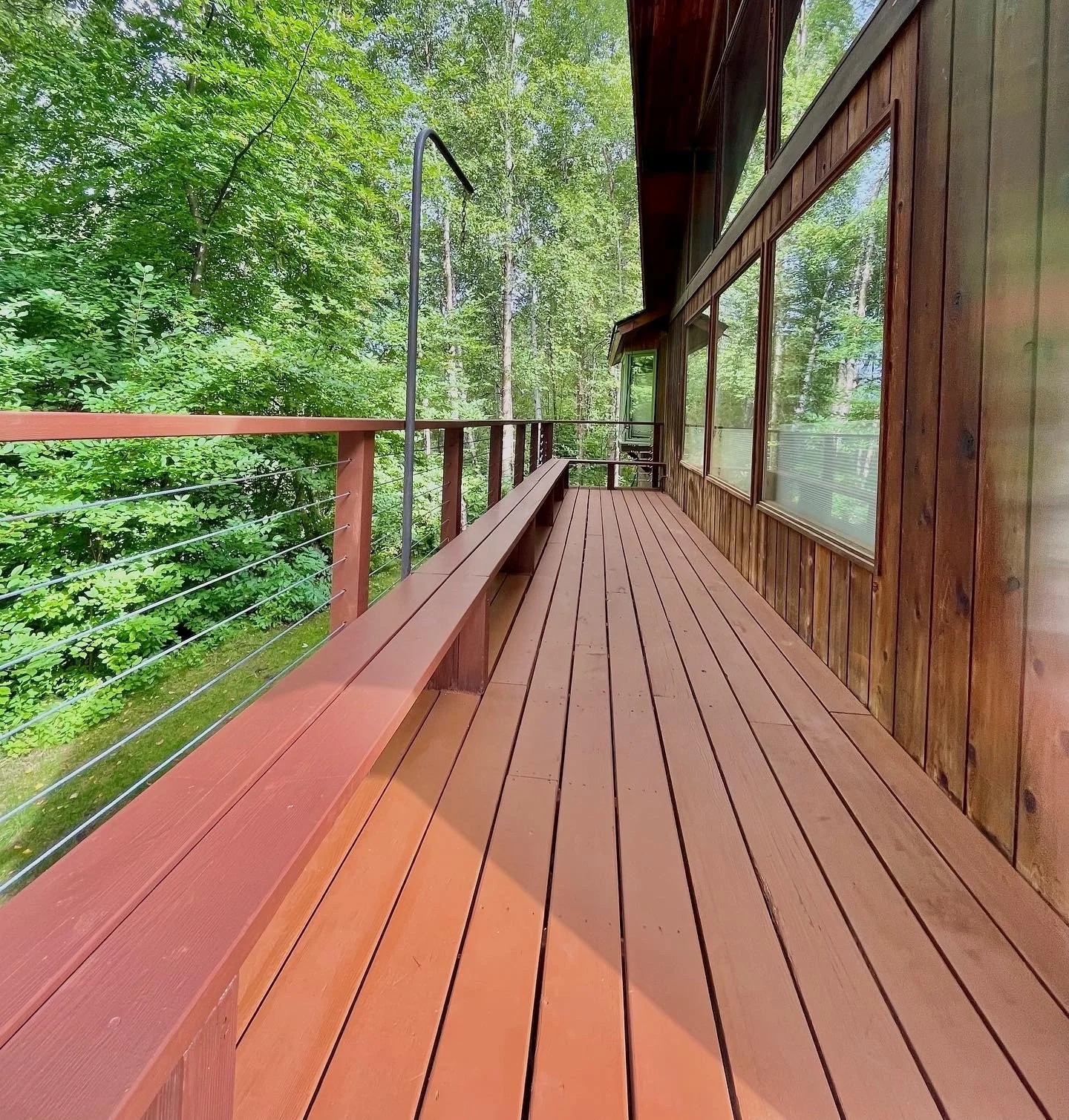 Wooden deck with railing surrounded by lush green trees.