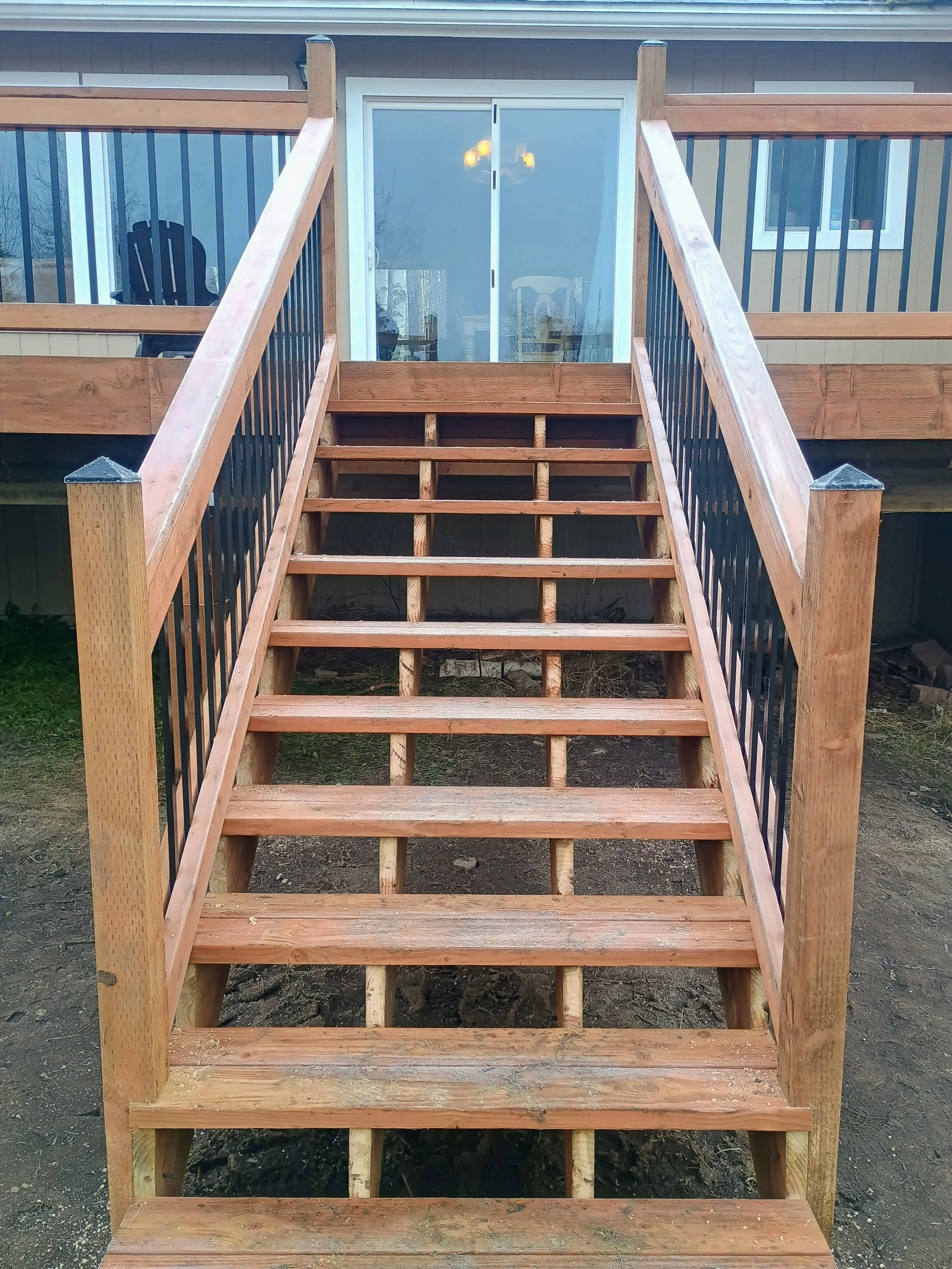 Wooden outdoor deck stairs with black metal railing leading up to a glass sliding door.