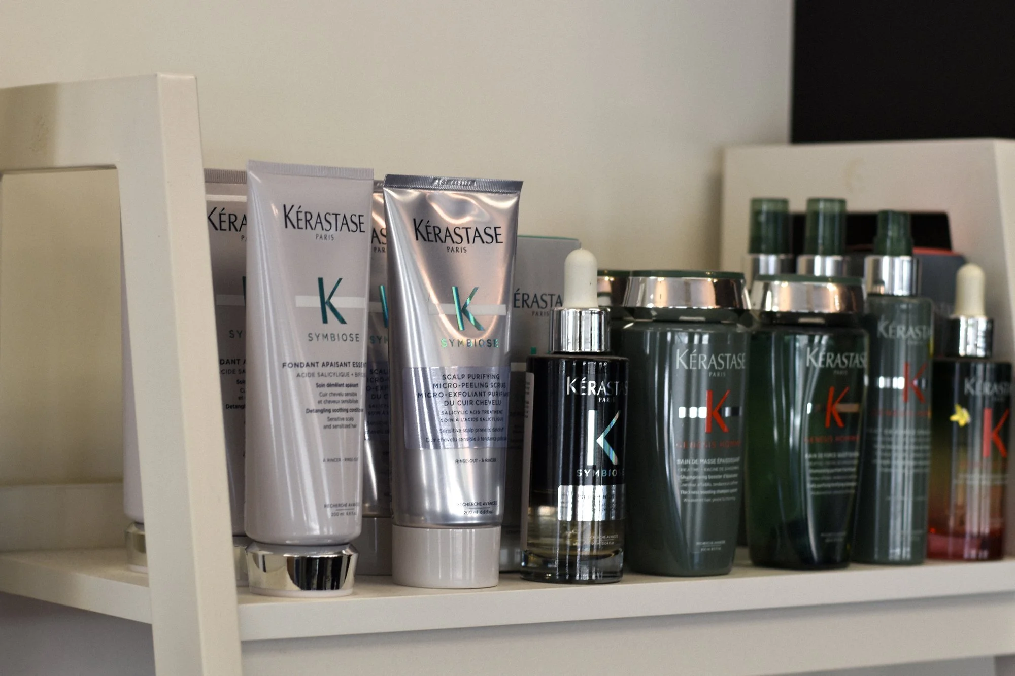 Shelf containing Kérastase Symbiose hair care products, including tubes, bottles, and jars in silver and dark green bottles.