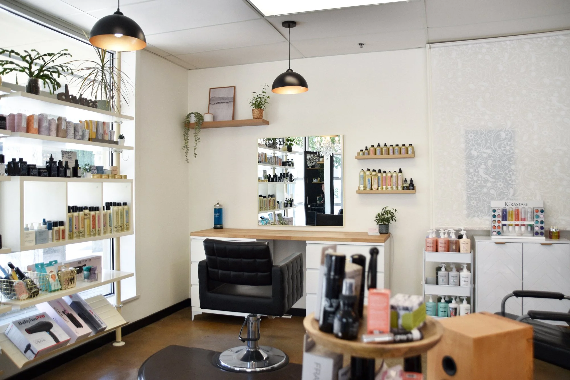 Interior of a beauty or skincare store with shelves holding bottles, lotions, and other products. There is a black chair, a mirror, shelves with plants, and ceiling lights.
