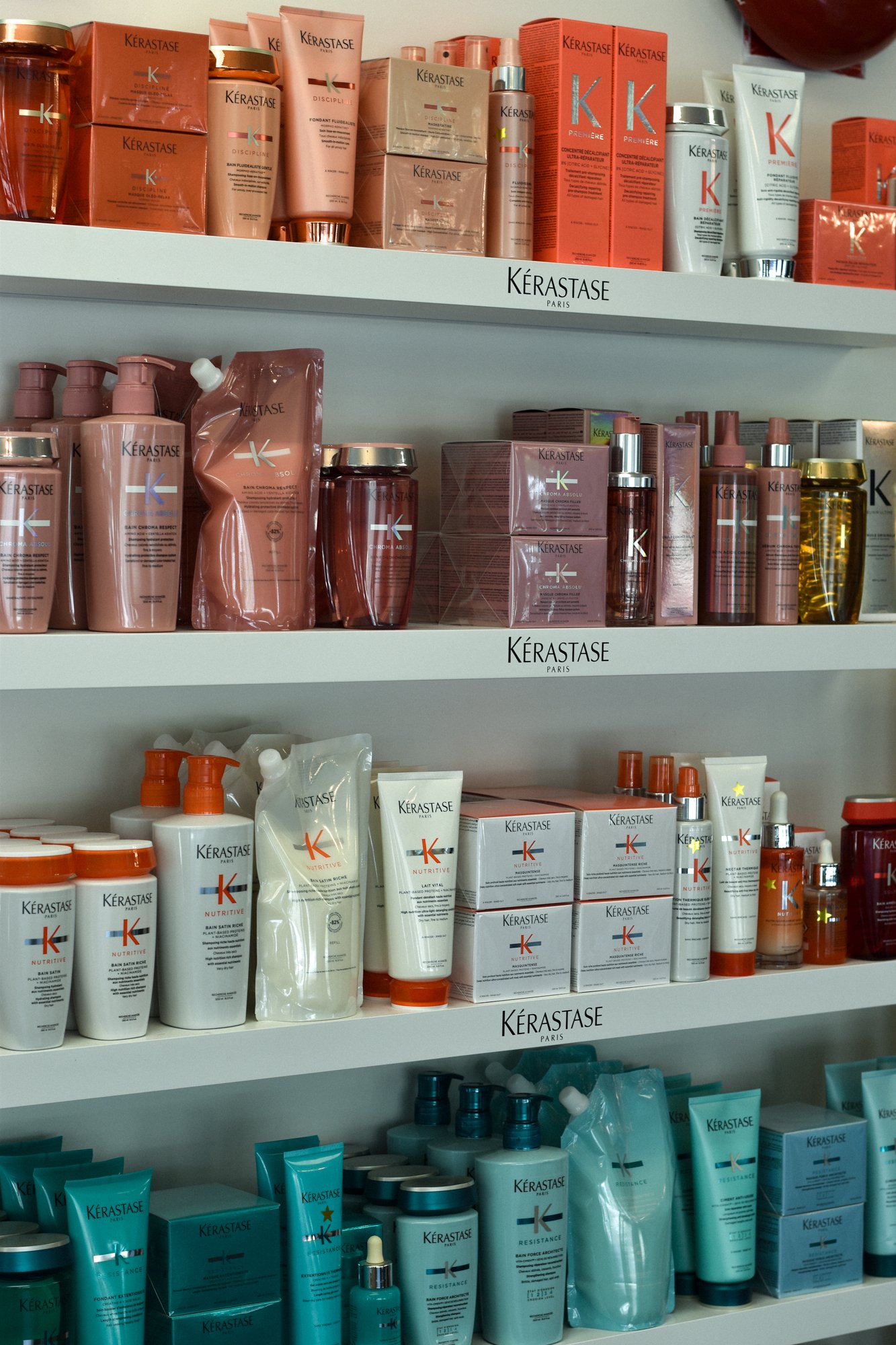 Shelves with various skincare and hair care products from Kérastase, including shampoos, conditioners, and treatments in different colored packaging.