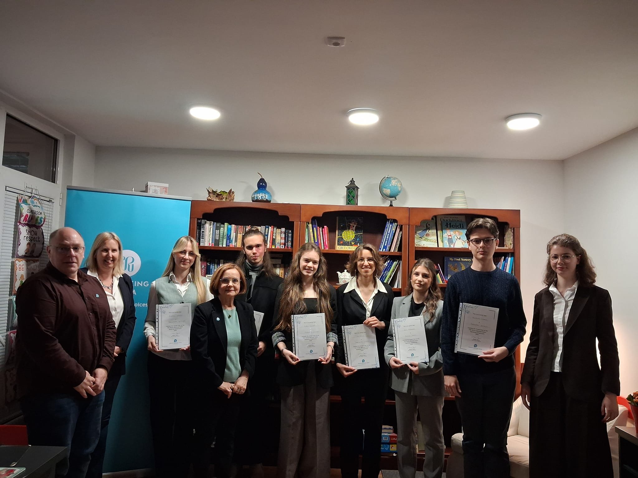 ESU Serbia team members with competition winners, standing in front of bookshelves and organization banner.
